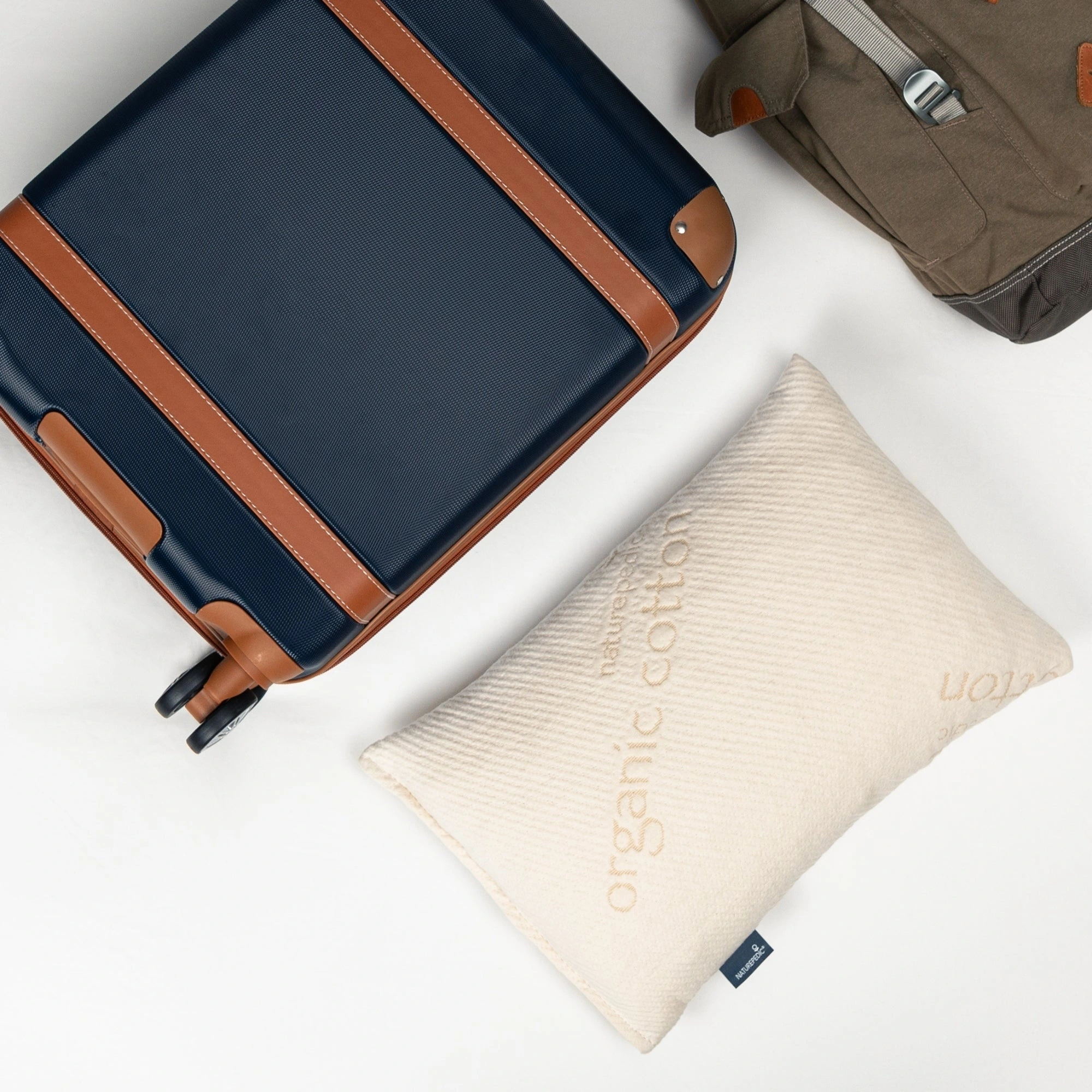 Naturepedic Organic Latex Travel Pillow beside a suitcase and travel bag